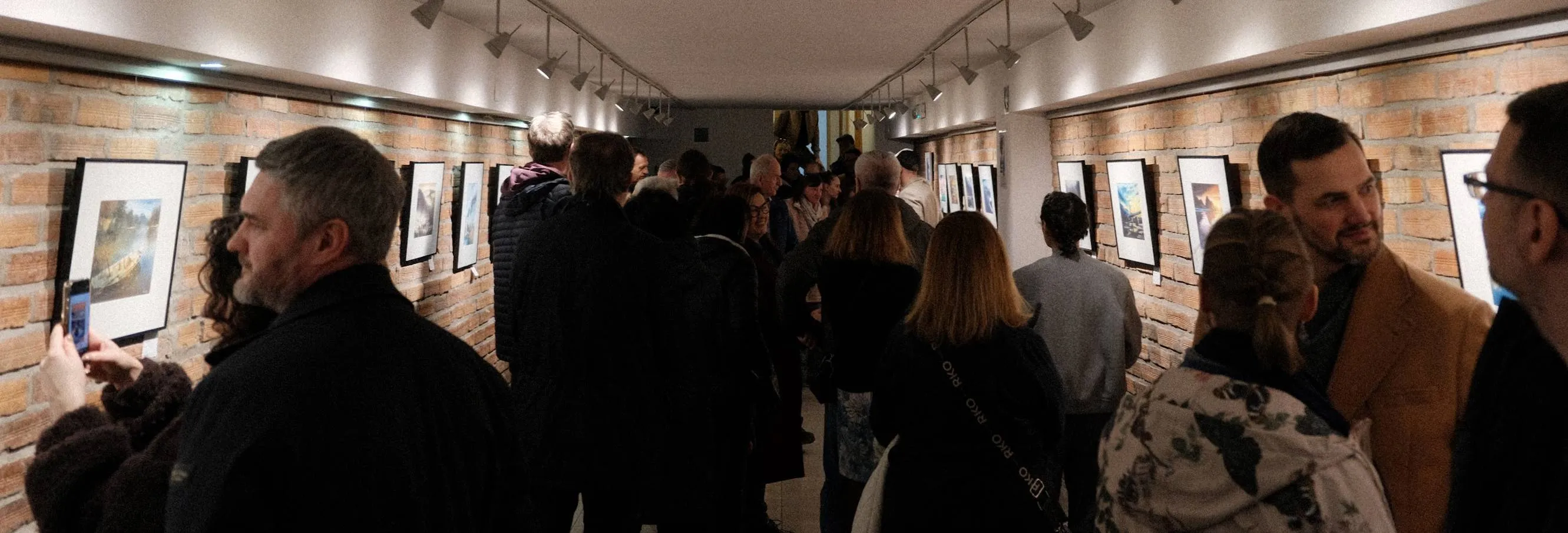 Galeria sztuki z ceglanymi ścianami i wiszącymi na nich obrazami, wypełniona przez ludzi na wernisażu